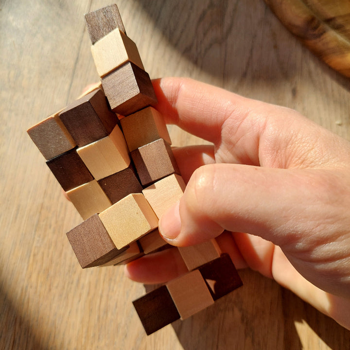 houten pocketpuzzel, tweekleuren hout puzzel slang in hand op houten tafel, sfeer foto, motoriekspeelgoed