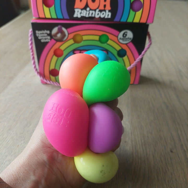 rainboh teenies van needoh, hand houd alls zes ballen vest en drukt. Op de tafel in de achtergrond de verpakking