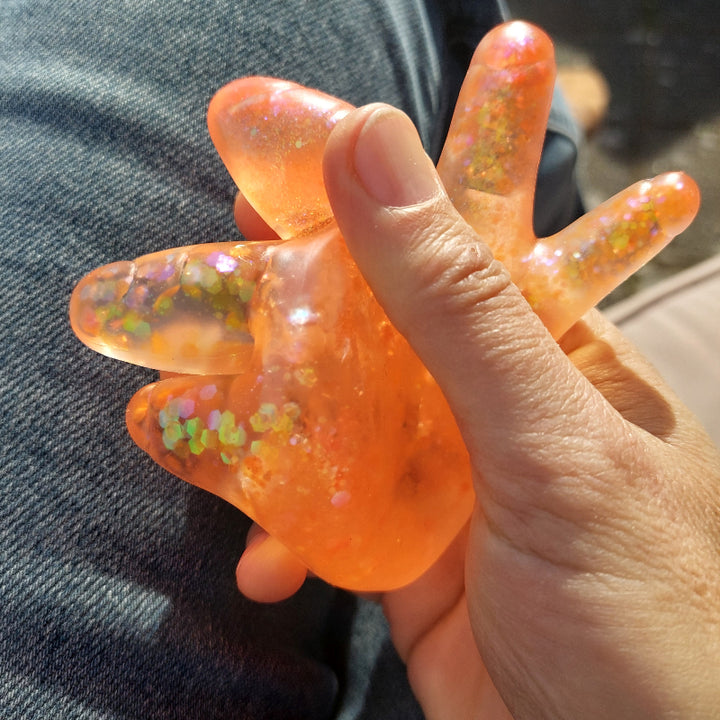 Sugar Squeeze hand, fidget hand oranje met glitter gedruk in een hand, zonlicht