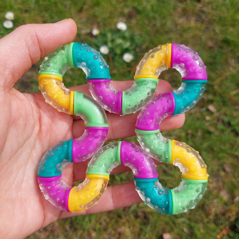 grote therapy tangle think in hand, kleuren paars, oranje, turquois en groen, achtergrond groen gras met bloemen