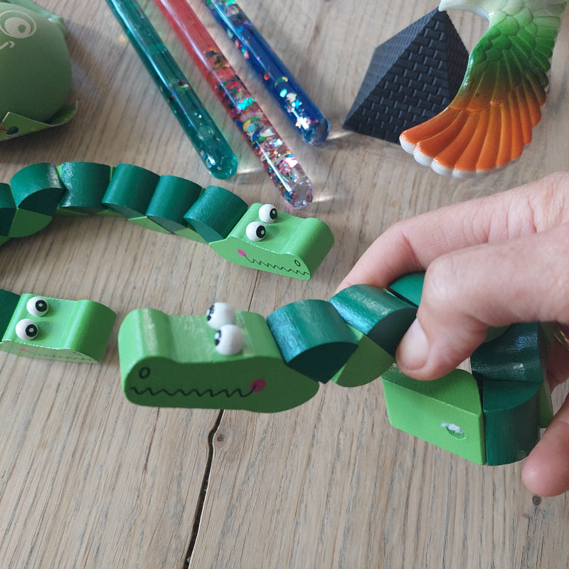 Hand met pocketpuzzel krokodil als afleiding bij een medische behandeling, terwijl de andere onderdelen van de afleidingsset op de achtergrond zichtbaar zijn.