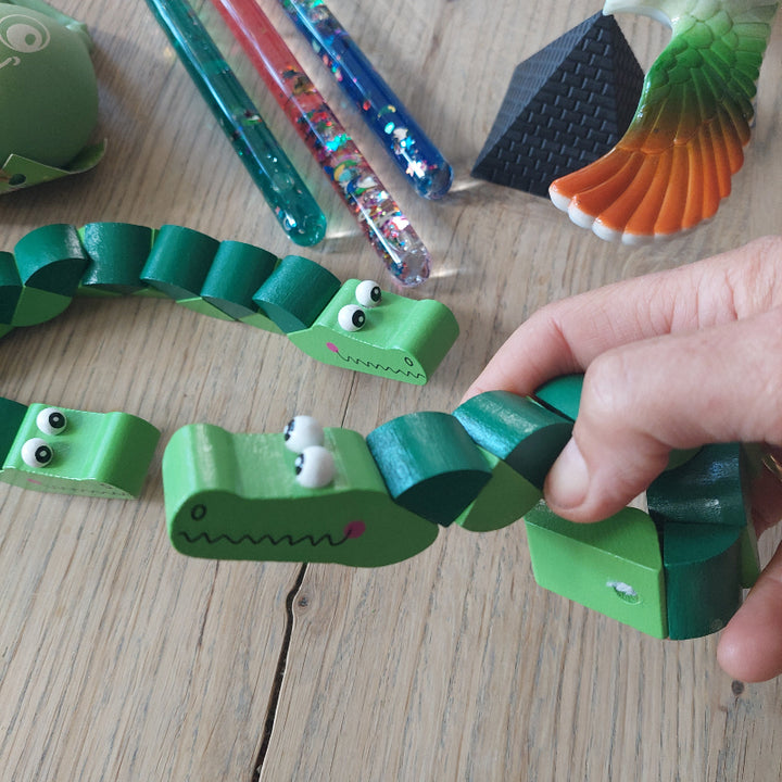 Hand met pocketpuzzel krokodil als afleiding bij een medische behandeling, terwijl de andere onderdelen van de afleidingsset op de achtergrond zichtbaar zijn.