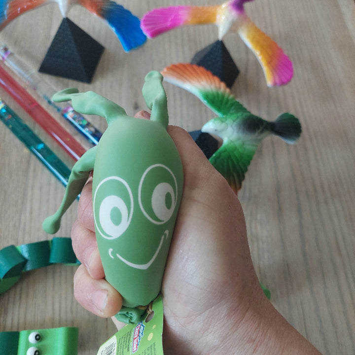 Hand knijpt in een stressbal gevuld met bioklei om spanning te verminderen tijdens een prikmoment, met de andere onderdelen van de afleidingsset op de achtergrond zichtbaar.