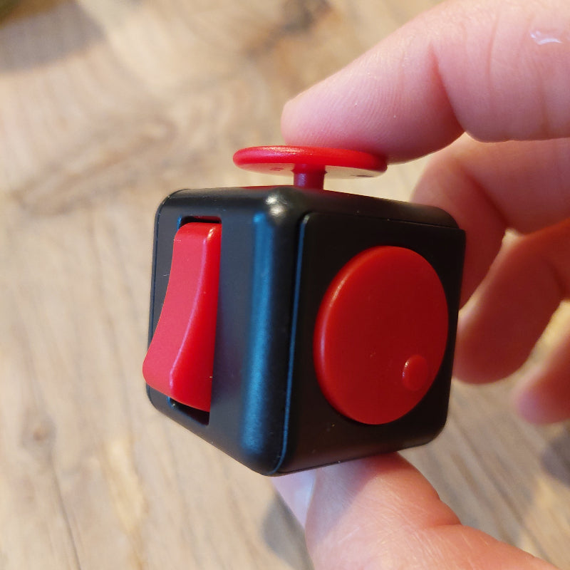 zwarte fidget cube in hand met rode schakelaars en knopen, fidget speelgoed, fijne motoriek materiaal vooe ergotherapie