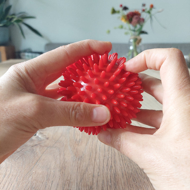 massagebal rot 8cm, in handen op houten tafel, bloemen op de achtergrond, sie materiaal webshop