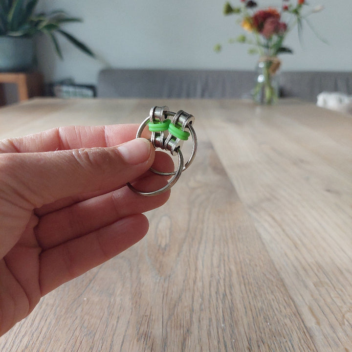fidget chain groen in hand, houten tafel, bloemen op achtergrond, fidgetspeelgoed, metal, sleutelhanger