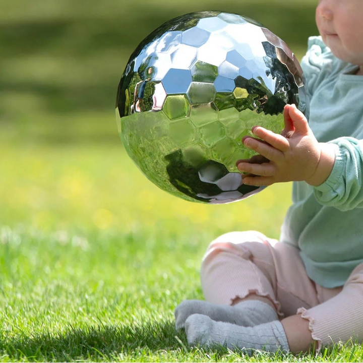 Een kind houdt de sensorische stalen bal met twee handen vast , sensoriek en grove motoriek speelmateriaal voor baby, peuter, kleuter