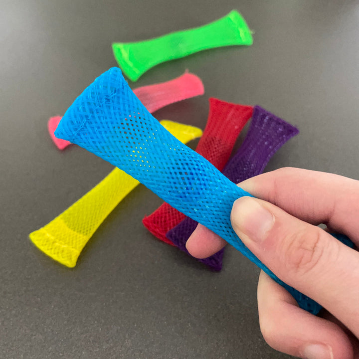 blauwe monkey fidget boink in hand, op de achtergrond de anderen kleuren uit het set, motoriekspeelgoed