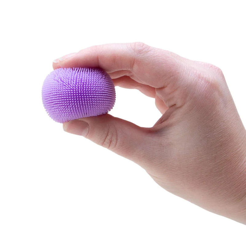 Hand die in een paarse NeeDoh Teenie Fuzz Ball knijpt met zachte velvet textuur