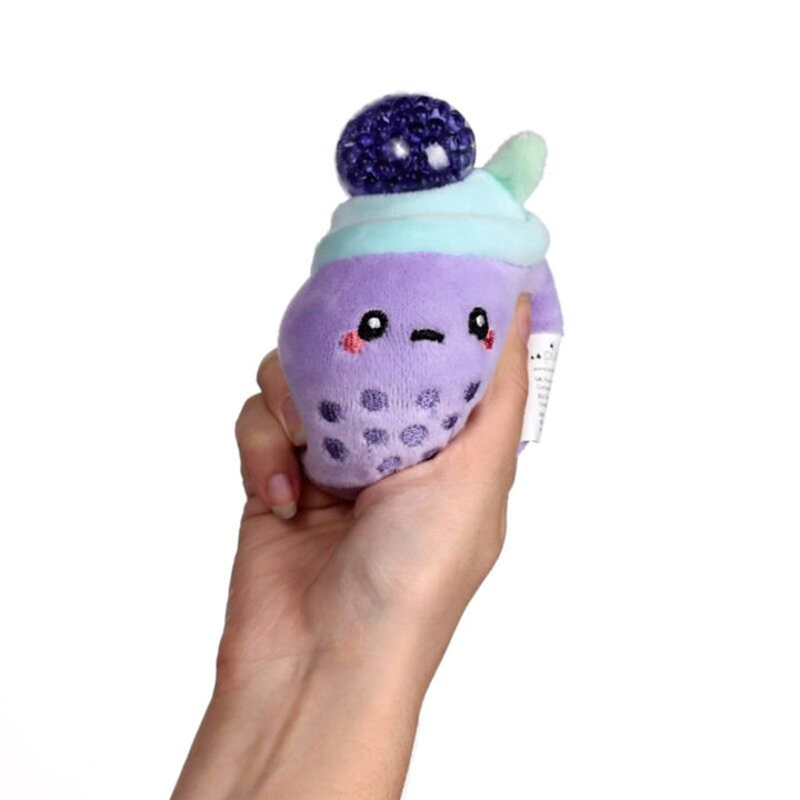 Hand knijpt in Queasy Squeezies waardoor de waterbead-bal bovenin naar buiten komt, paars, taro, boba thee fidget, foodimals