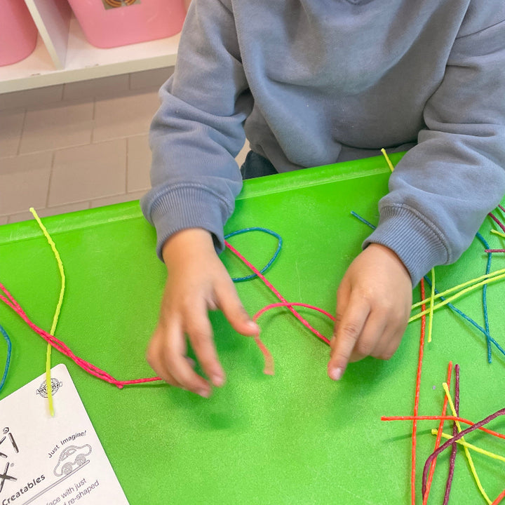 handen die Wikki Stix in neonkleuren gebruiken tijdens knutselen