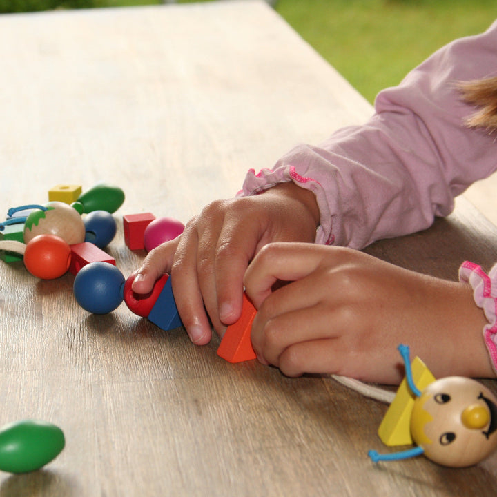 Kinderhanden zoeken de juiste houten vorm bij de kleur- en vormdobbelsteen tijdens het spel Rondo Vario.
