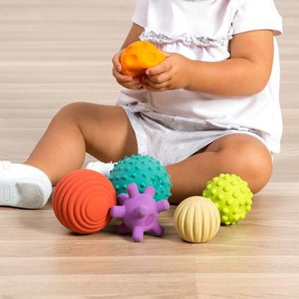 Tkind met de set rubber baby ballen – sensorisch speelgoed voor fijne en grove motoriek, kind heeft oranje bal in de hand en drukt