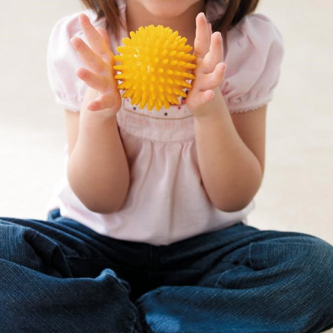 weplay Massagebal 8cm geel, kind houd de bal met twee handen vast, sensoriek spel