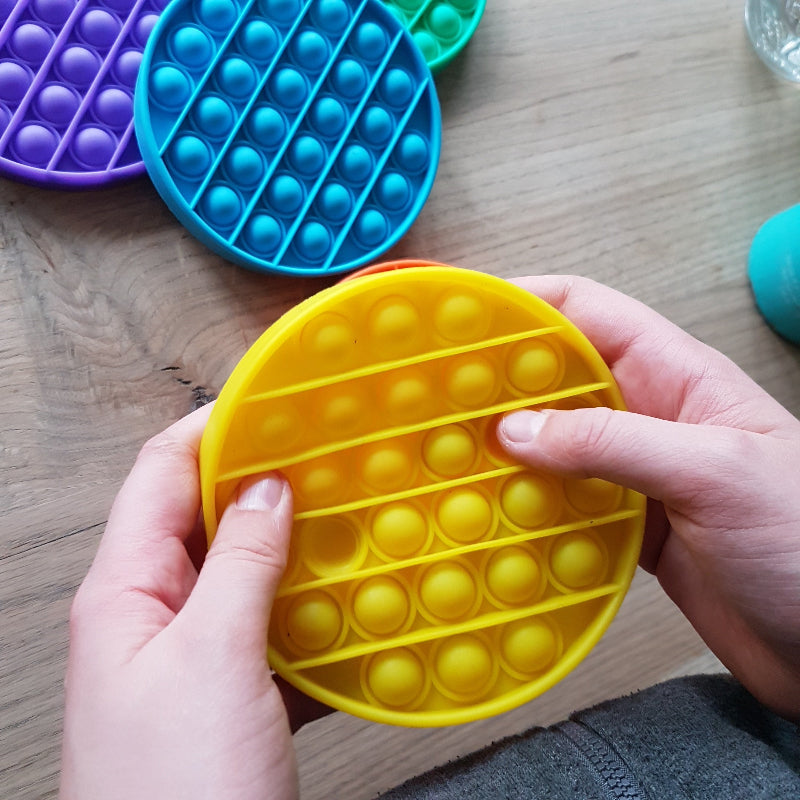 Toys42Hands Pop it rondm gele pop it met twee handen vast gehouden, motoriekspeelgoed