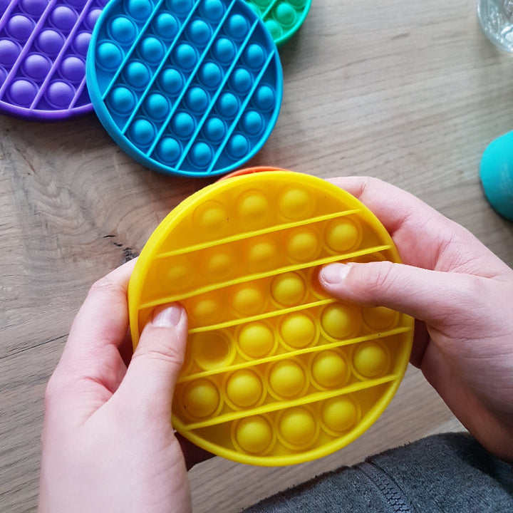 Toys42Hands Pop it rondm gele pop it met twee handen vast gehouden, motoriekspeelgoed