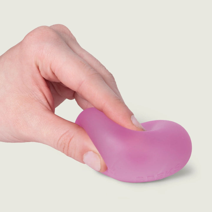 SPEKS Gump Original stressbal in kleur Moon Jelly roze, hand drukt de bal op tafel, toont soepele en kneedbare structuur, fidget